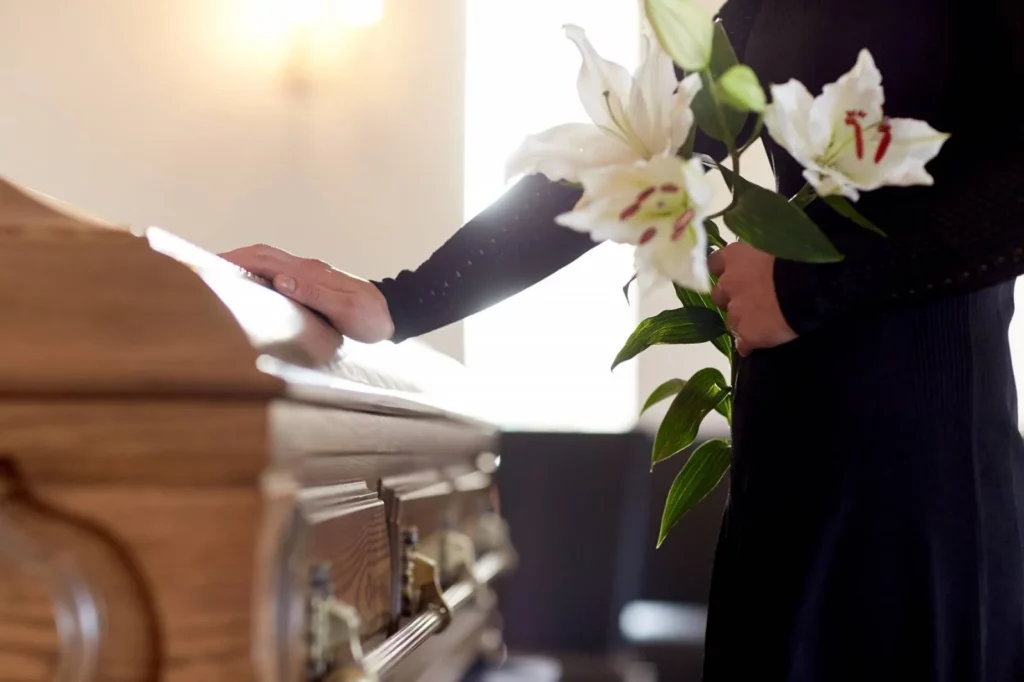 Main posée avec respect sur un cercueil en bois et bouquet de lillies blanches