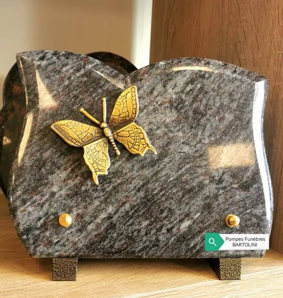 Plaque funéraire en granit gris veiné surmontée d'un papillon en bronze