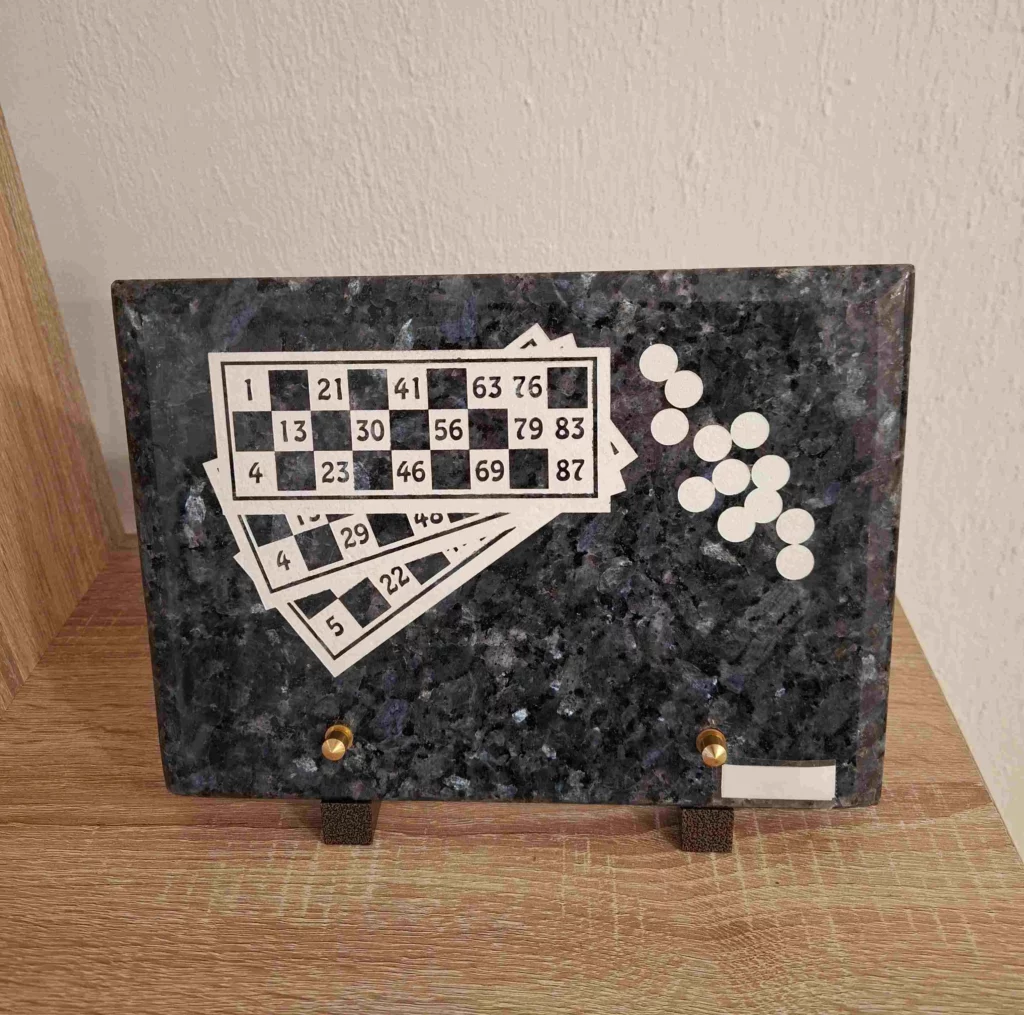 Plaque funéraire en granit bleu gravée de cartes de loto et jetons de jeu