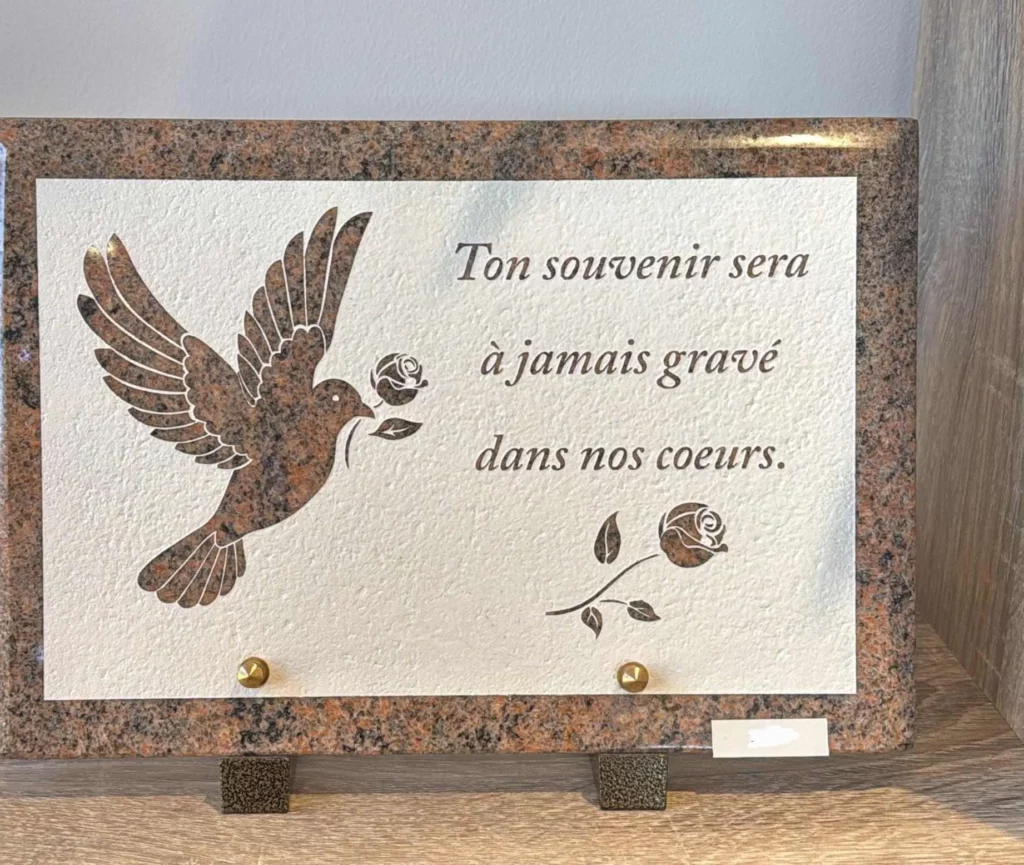 Plaque funéraire en granit beige gravée d'une colombe apportant une rose