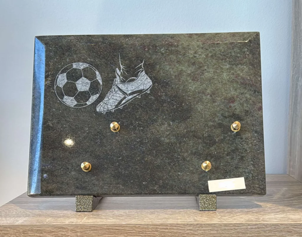Plaque funéraire rectangulaire en granit illustrée d'un joueur frappant dans un ballon