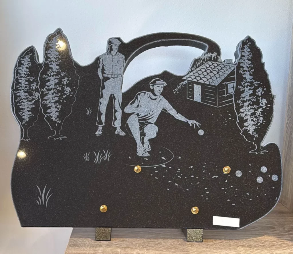 Plaque funéraire en granit noir gravée de joueurs de pétanque près d'un cabanon