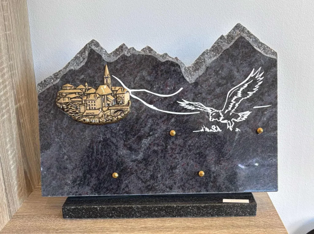 Plaque funéraire en granit découpée en forme de chaîne de montagnes avec rapace gravé