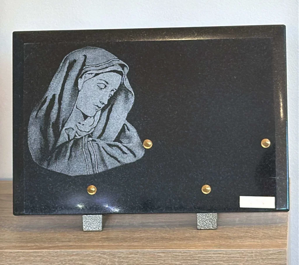 Plaque funéraire rectangulaire en granit noir gravée d'un visage de Vierge Marie
