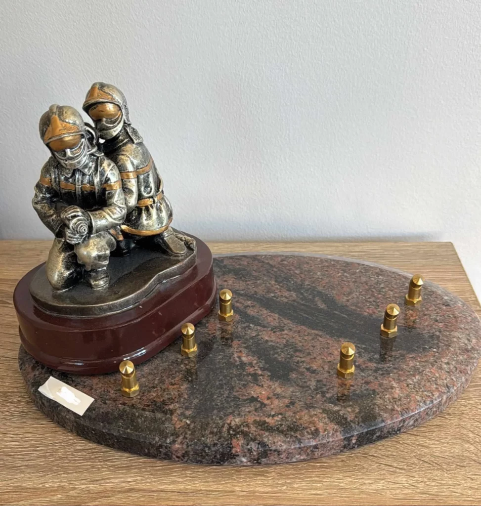 Plaque funéraire avec figurine de pompiers tenant une lance à eau sur socle