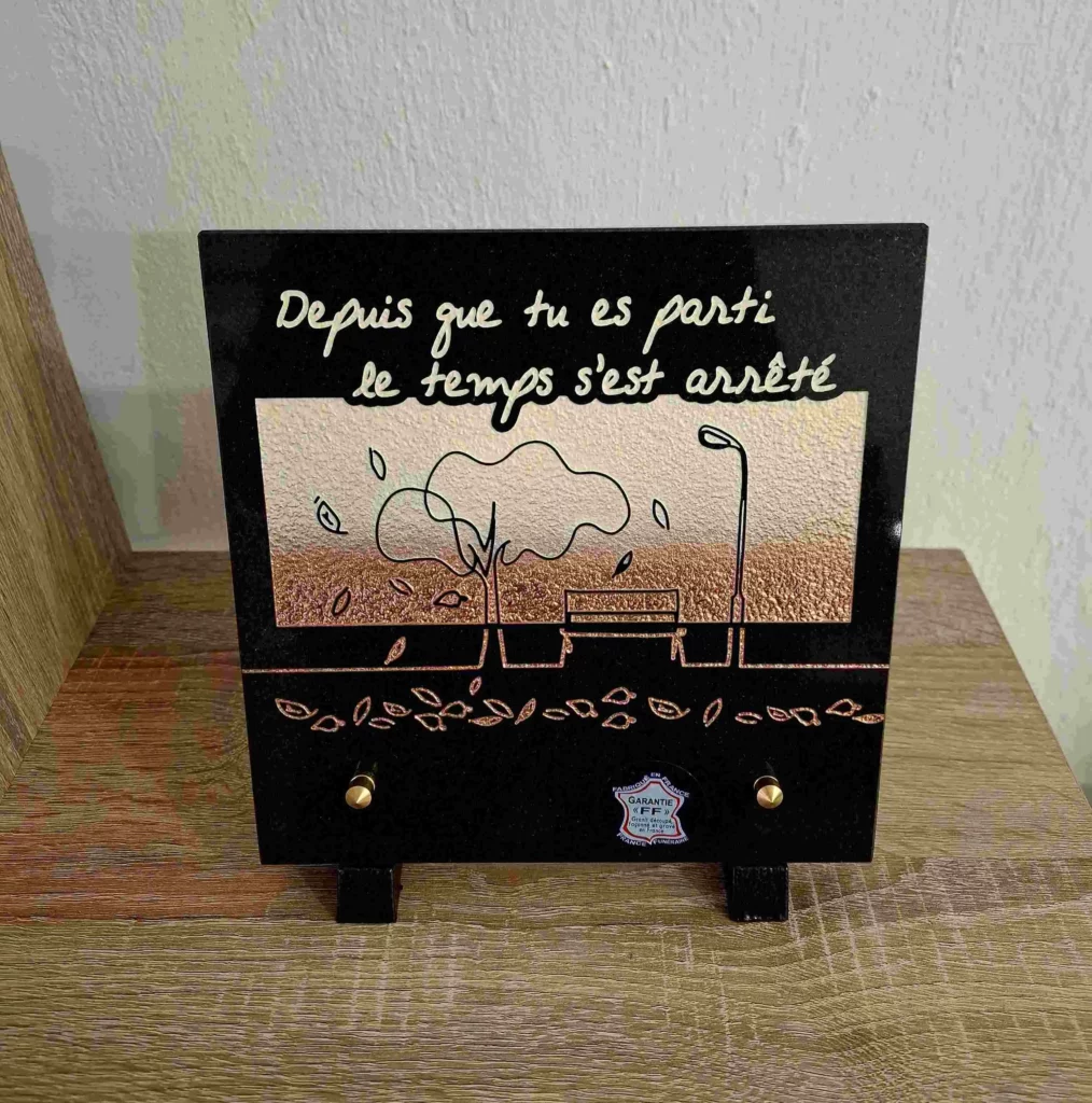 Plaque funéraire rectangulaire en granit avec gravure de paysage et banc sous un arbre