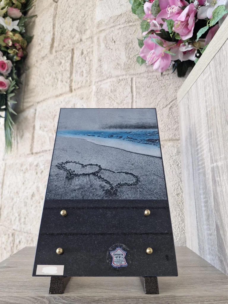 Plaque funéraire rectangulaire illustrée d'une plage avec deux cœurs dessinés dans le sable