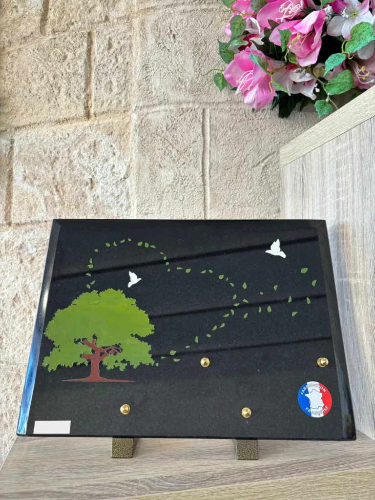 Plaque funéraire en granit noir illustrée d'un arbre et d'un envol d'oiseaux en cœur